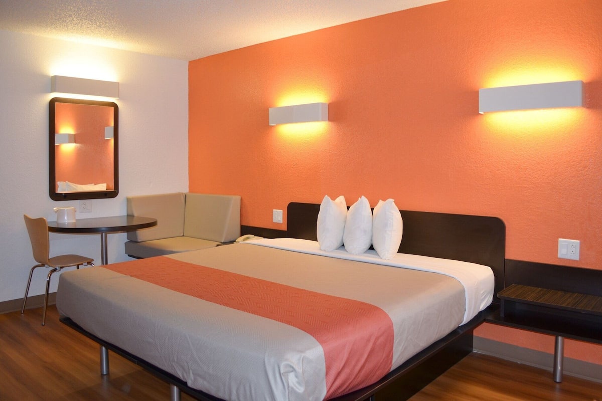 A hotel room with a bed, a desk, a chair, and a small table.