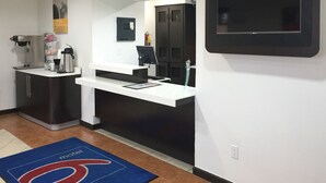 A modern hotel room with a kitchenette, a flat-screen TV, and a blue carpet with a logo. - Motel 6 Kingsland, GA - Kings Bay Naval Base (Kingsland)