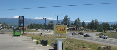 Blick an einer Straße mit Schild eines Pizza Restaurants, einer Tankstelle und einem kleinen, grünen Gebäude.
