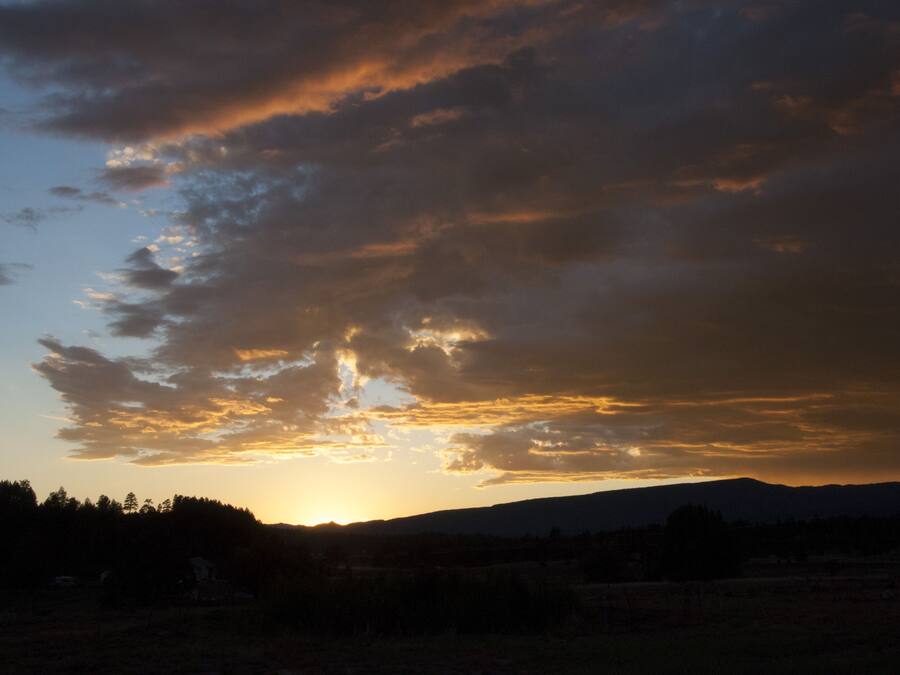 A sunset over a mountainous landscape with a silhouette of trees and a flat field.