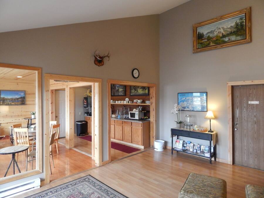 A spacious living area with wooden flooring, a dining table with chairs, a kitchen area with wooden cabinets, a mounted deer head, and a painting on the wall.