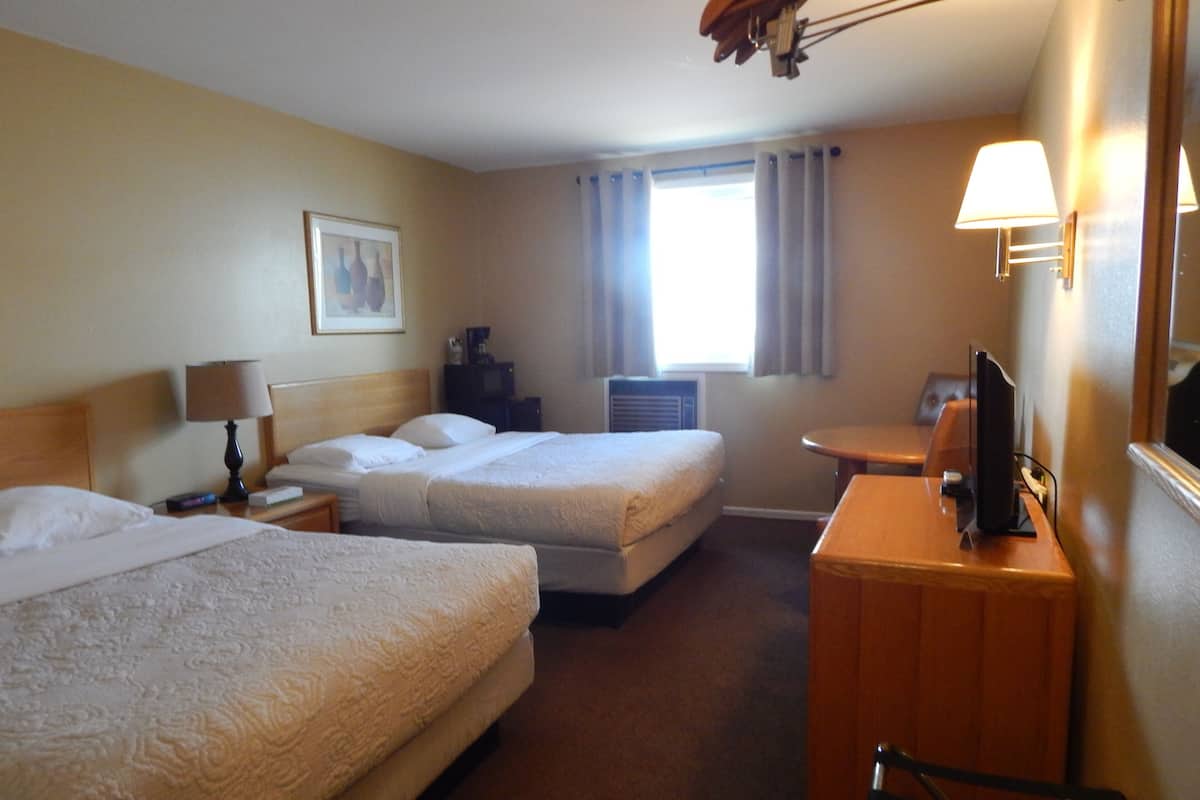A hotel room with two beds, a desk with a lamp, a television, and a window with curtains.