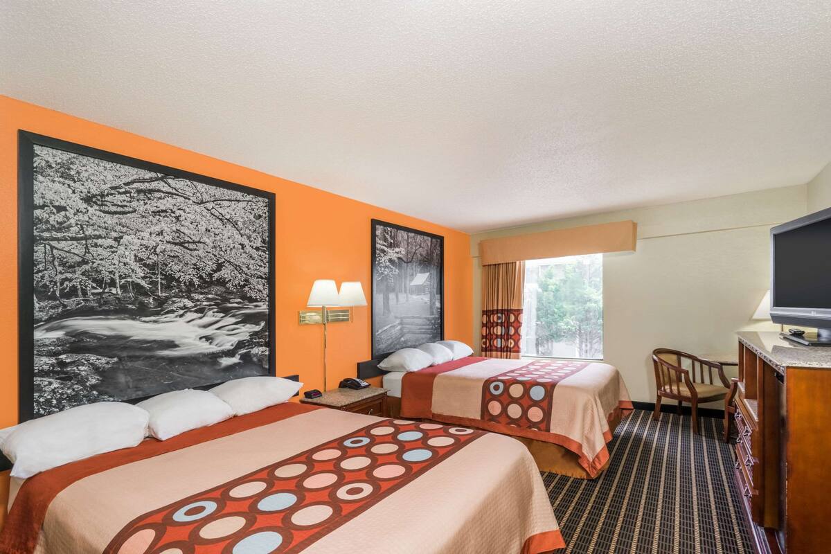 Een hotelkamer met twee bedden, een televisie, een bureau en een groot raam.