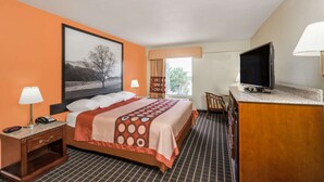 Una habitación de hotel con cama, escritorio, televisor y ventana con cortinas.