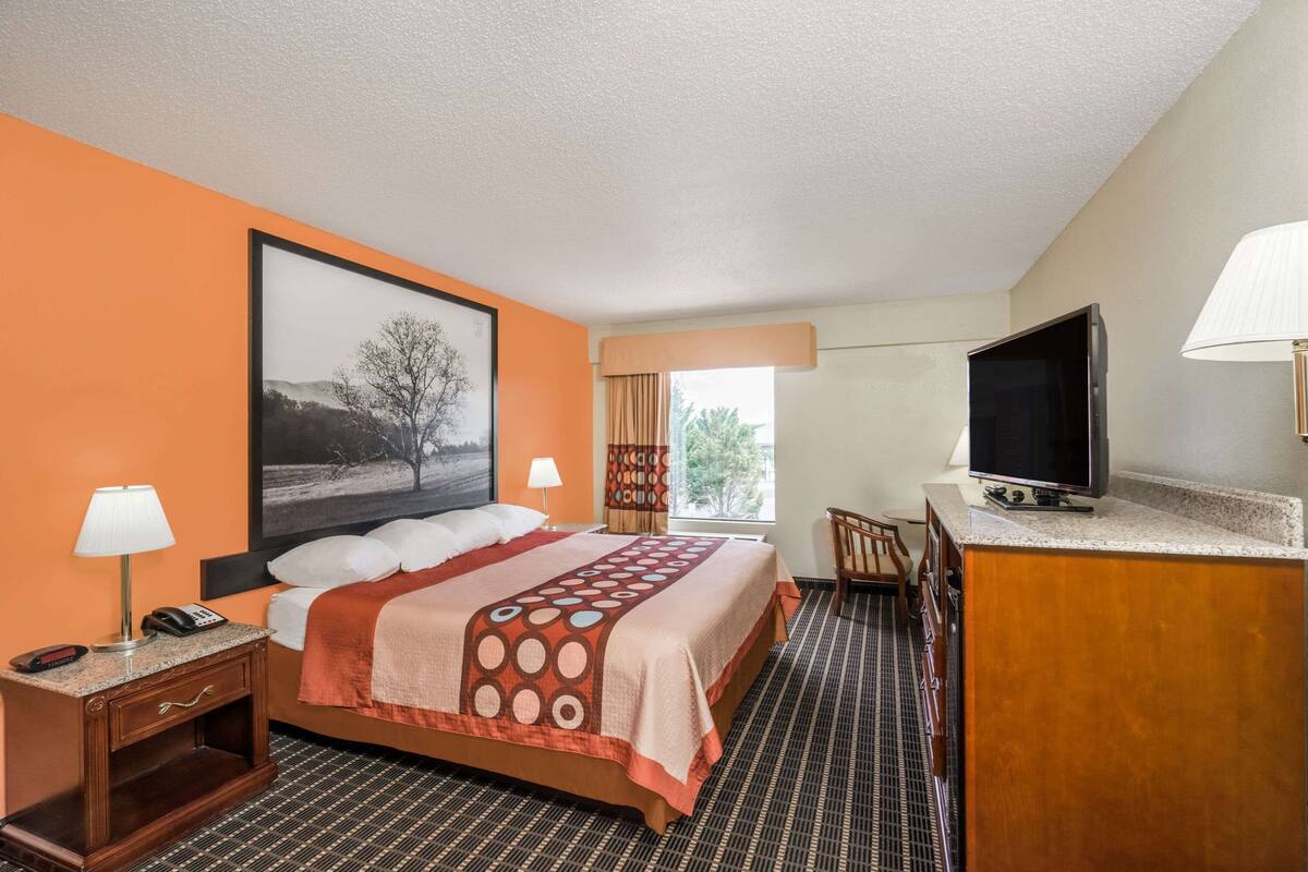 Een hotelkamer met een bed, bureau, televisie en een raam met gordijnen.