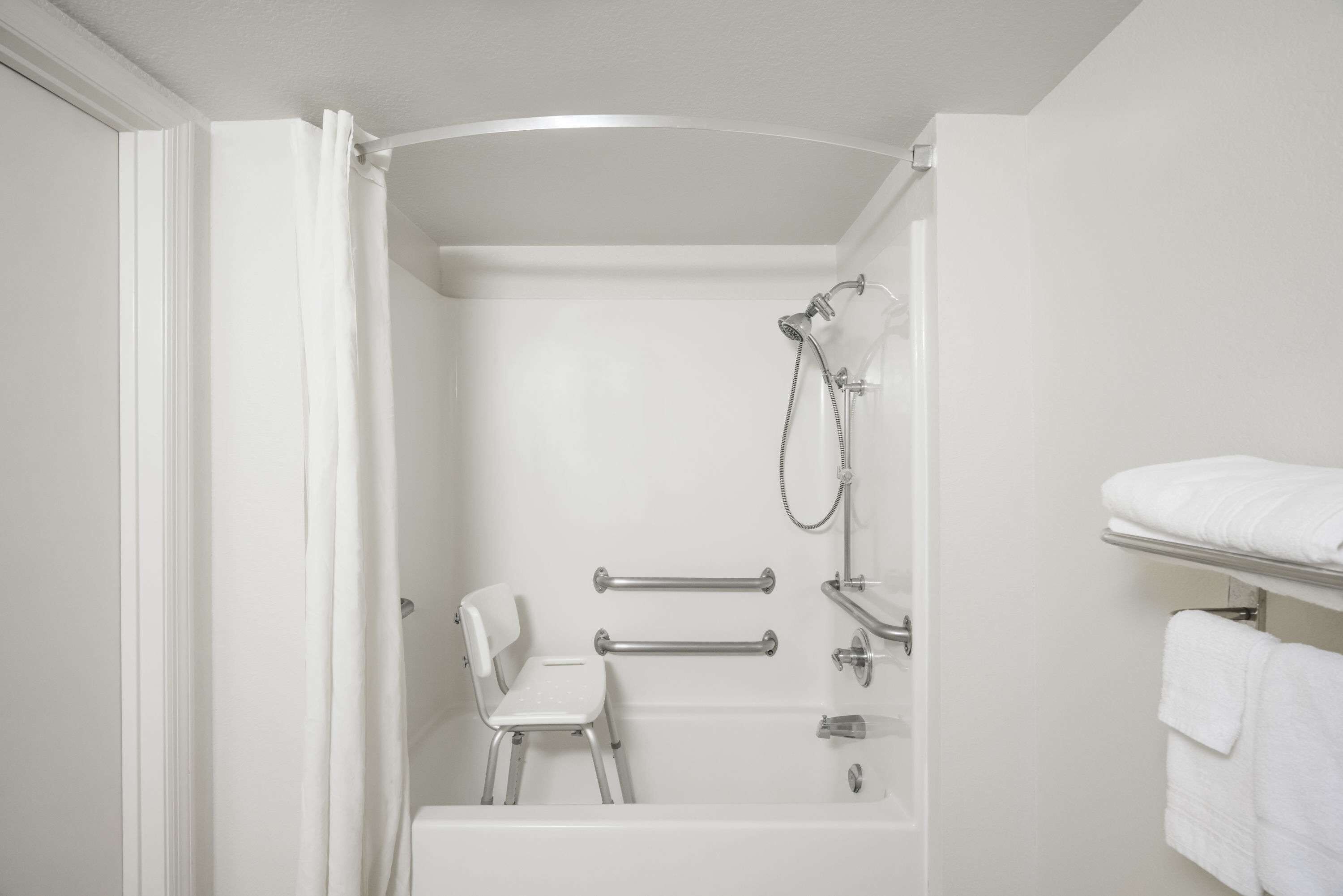 Een witte badkamer met een douche, een witte stoel en een handdoekhouder.