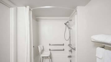 A white bathroom with a shower, a white chair, and a towel rack.