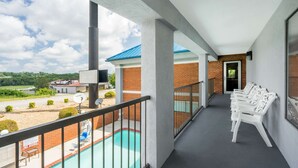 Un balcón con piscina, sillas blancas y vista a un edificio de techo azul.