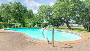 A swimming pool with a metal ladder, surrounded by a pebble deck and trees. - Super 8 by Wyndham San Antonio/Fiesta (San Antonio)