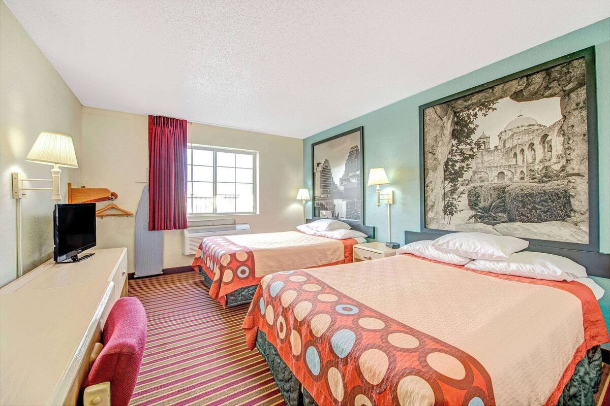 Ein Hotelzimmer mit zwei Betten, einem Schreibtisch, einem Fernseher und einem großen gerahmten Bild an der Wand.
