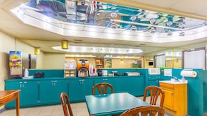 A restaurant with teal cabinets, wooden chairs, a glass ceiling, and a microwave.