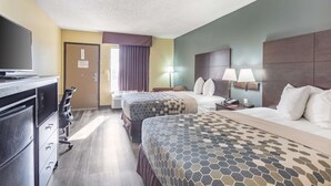 A hotel room with two beds, a desk with a television, and a dresser.