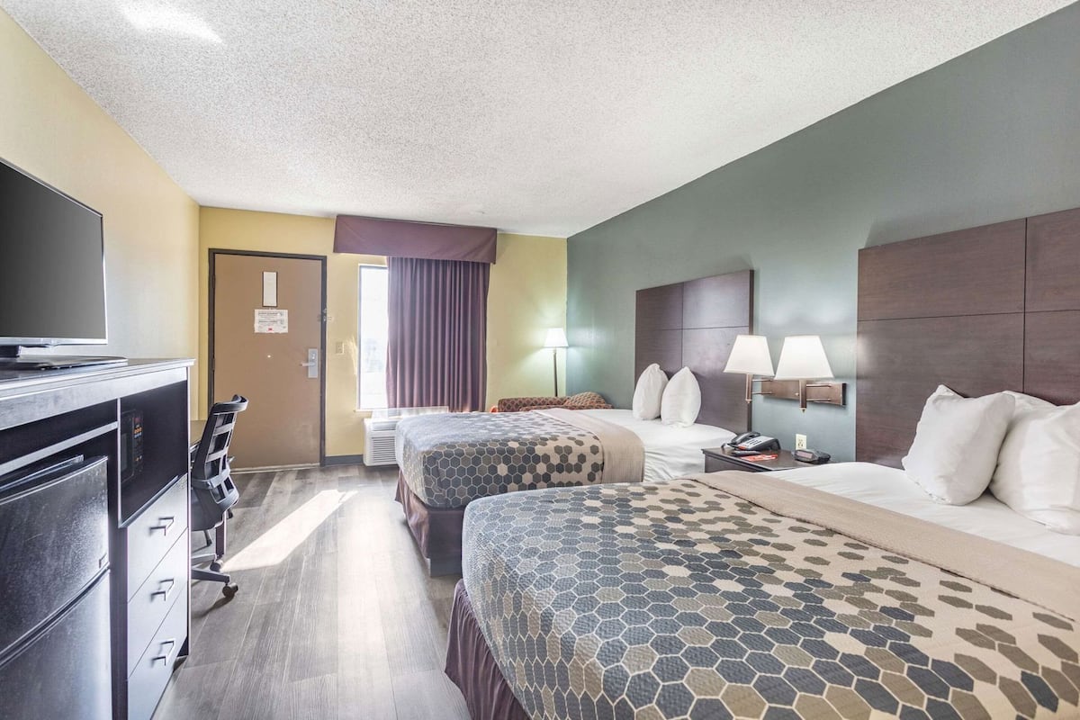 A hotel room with two beds, a desk with a TV, a chair, and a window with curtains.