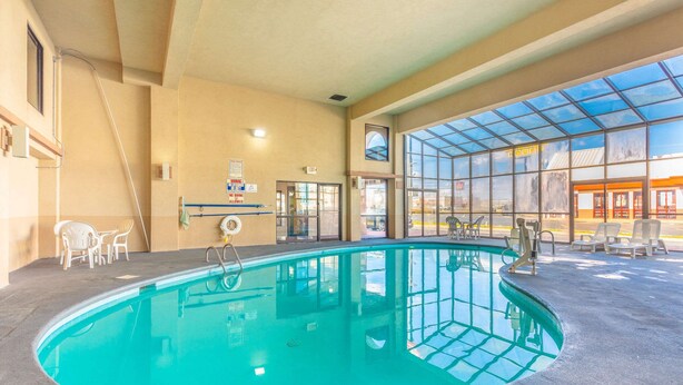 An indoor swimming pool with clear glass walls, a tiled floor, and a few lounge chairs.