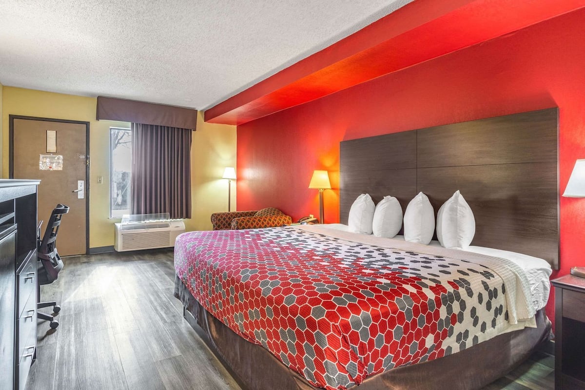 A hotel room with a bed, a desk, a chair, a lamp, and a window with curtains.