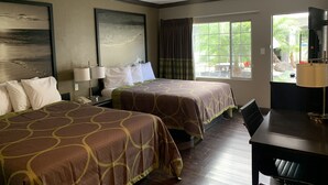 Ett hotellrum med två sängar, ett skrivbord och ett fönster med utsikt över grönområden.