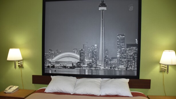 A hotel room with a bed, two bedside lamps, a framed cityscape picture on the wall, and a telephone on the nightstand.