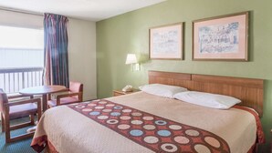 A hotel room with a bed, a desk, a chair, a nightstand, and two framed pictures on the wall.