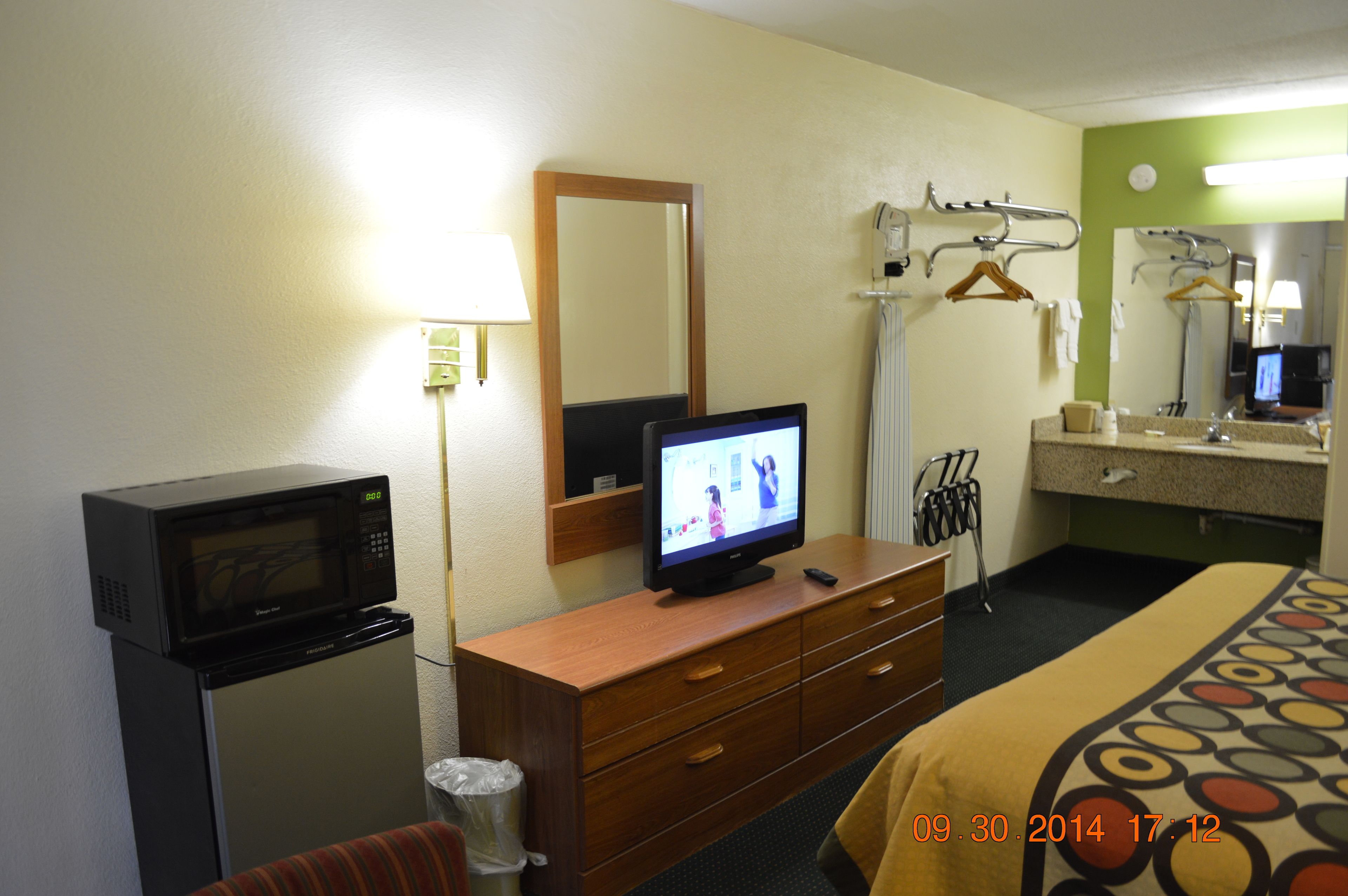 A hotel room with a microwave, television, wooden dresser, and a bed with a patterned bedspread.