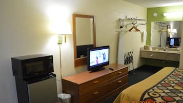 A hotel room with a microwave, television, wooden dresser, and a bed with a patterned bedspread.