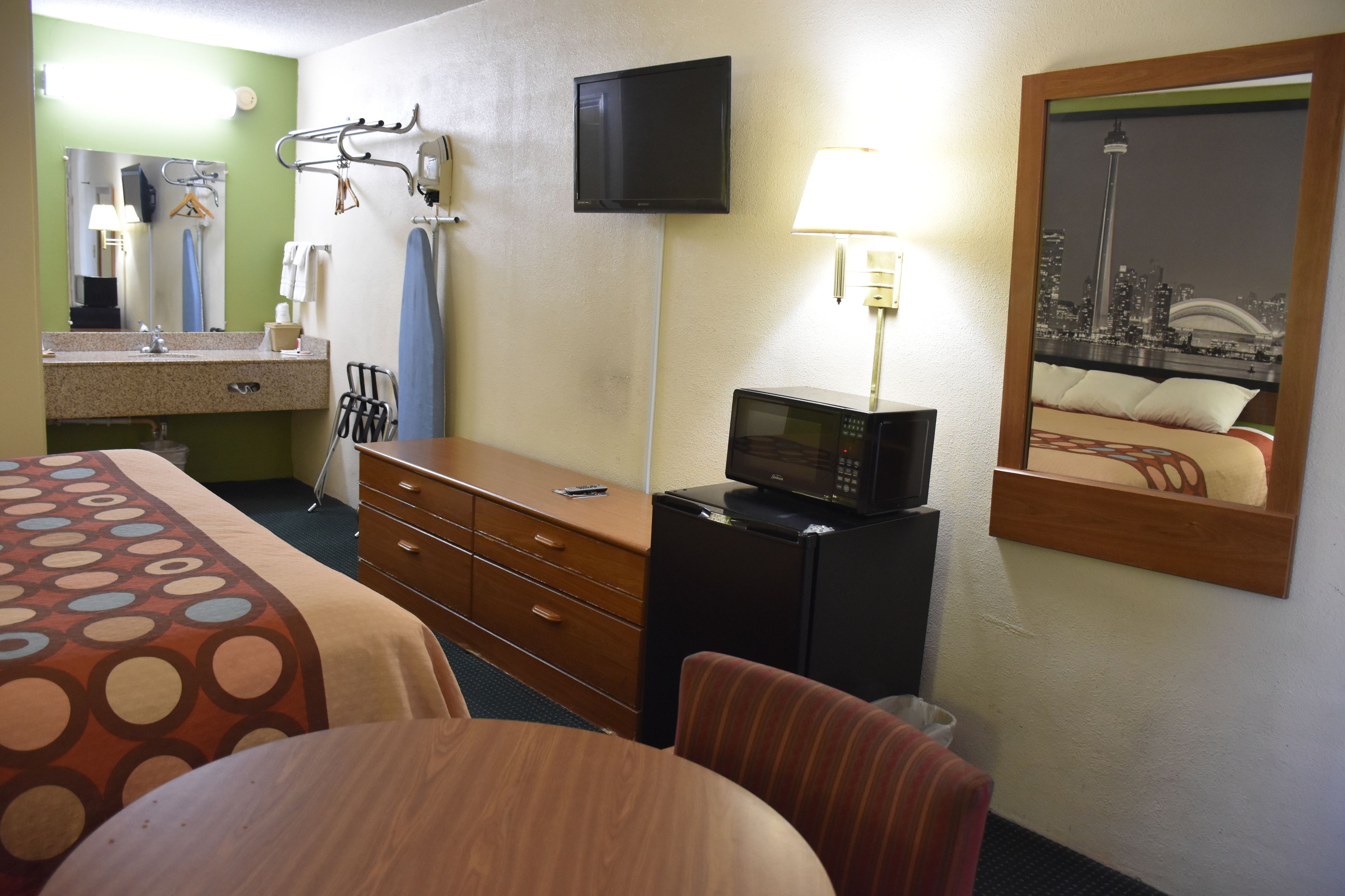 A hotel room with a bed, a desk with a computer, a TV, a microwave, and a cityscape mirror.