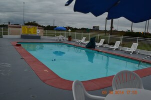 Una piscina con borde rojo, sillas reclinables blancas y un cartel con las normas de la piscina.