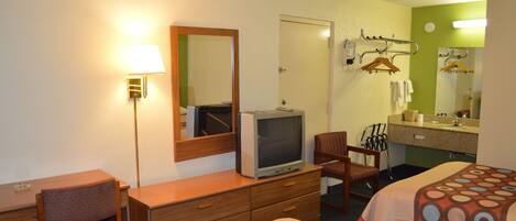 Hotellihuone, jossa on sänky, työpöytä, tuoli, lipasto, televisio, peili sekä kylpyhuone, jossa on pesuallas ja pyyhekoukku.