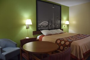 Un cuarto de hotel con una cama, dos sillas, una mesita y un cuadro de un paisaje urbano en la pared.