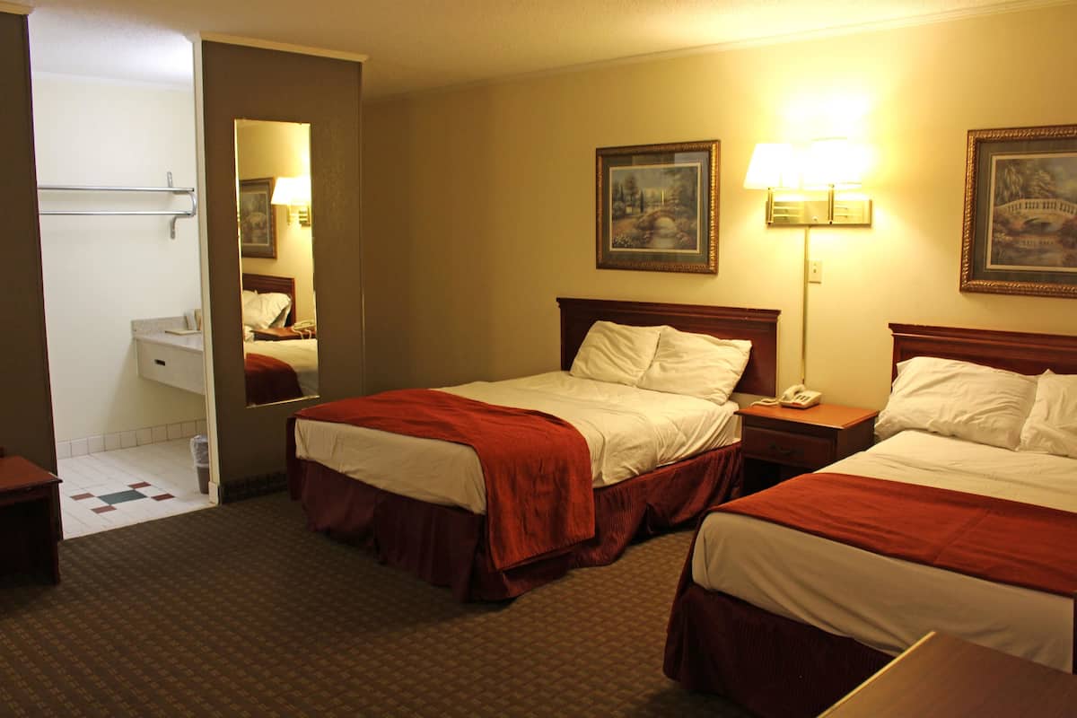 Een hotelkamer met twee bedden, een badkamer en een nachtkastje met een lamp.