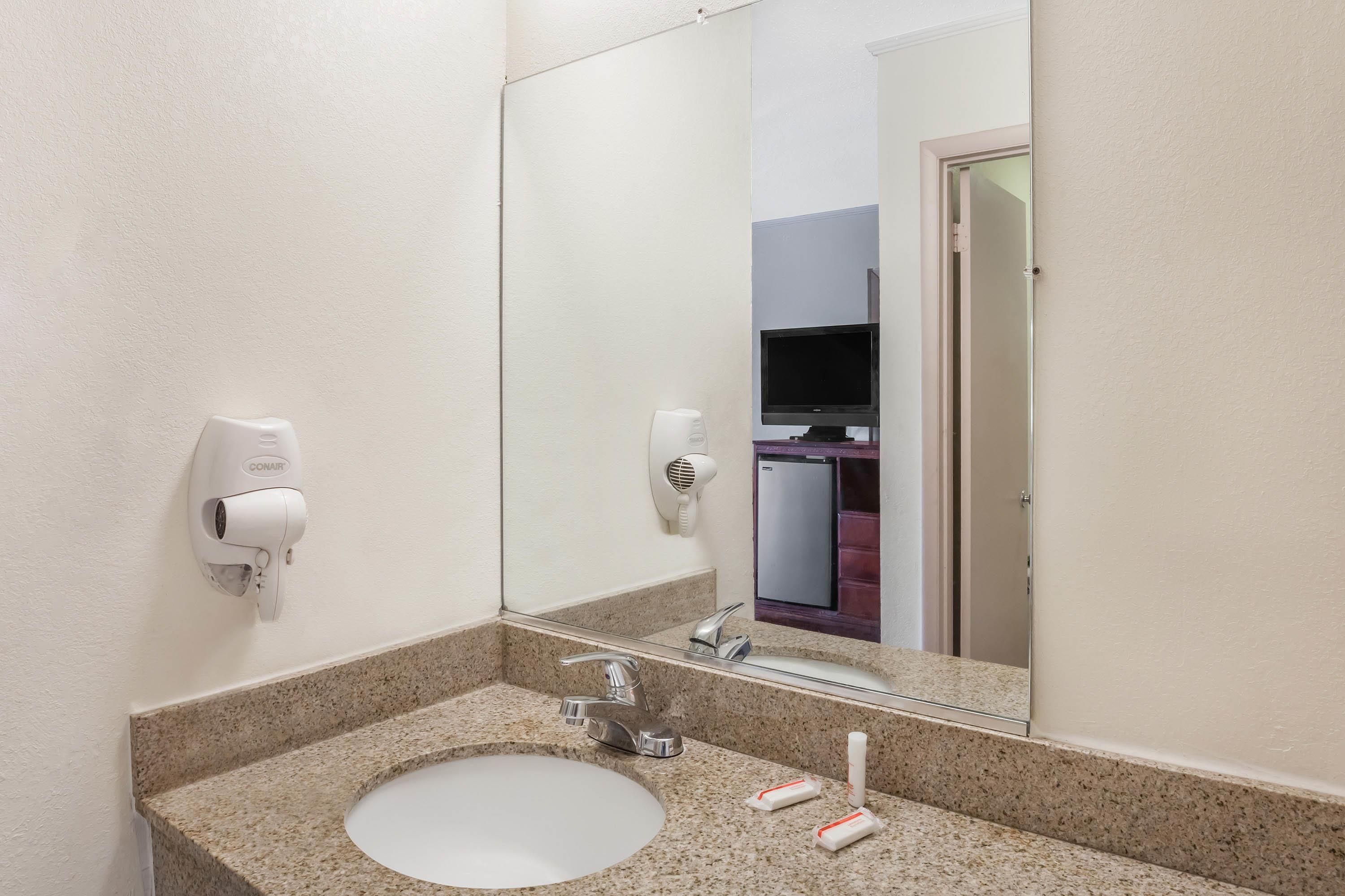 A bathroom with a granite countertop, a sink, a mirror, a hairdryer, and a hand dryer.