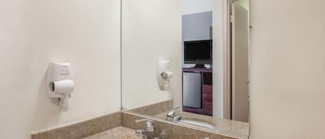 A bathroom with a granite countertop, a sink, a mirror, a hairdryer, and a hand dryer.