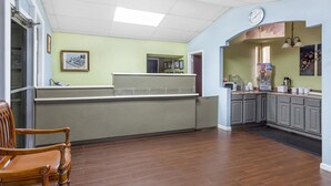 A spacious room with a wooden floor, a reception desk, a clock, and a kitchen area with cabinets and appliances.