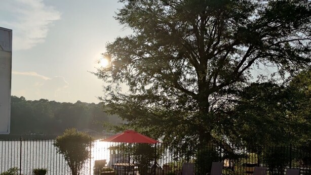 A swimming pool with a clear view of the sunset, surrounded by lounge chairs and a red umbrella.