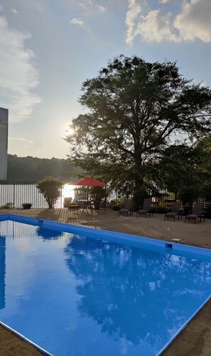 Una piscina con vistas despejadas al atardecer, rodeada de sillas de descanso y una sombrilla roja.