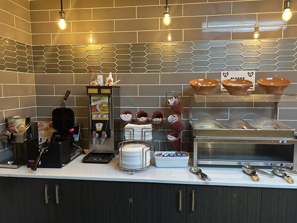A breakfast bar with waffle makers, syrup dispensers, and a coffee machine.