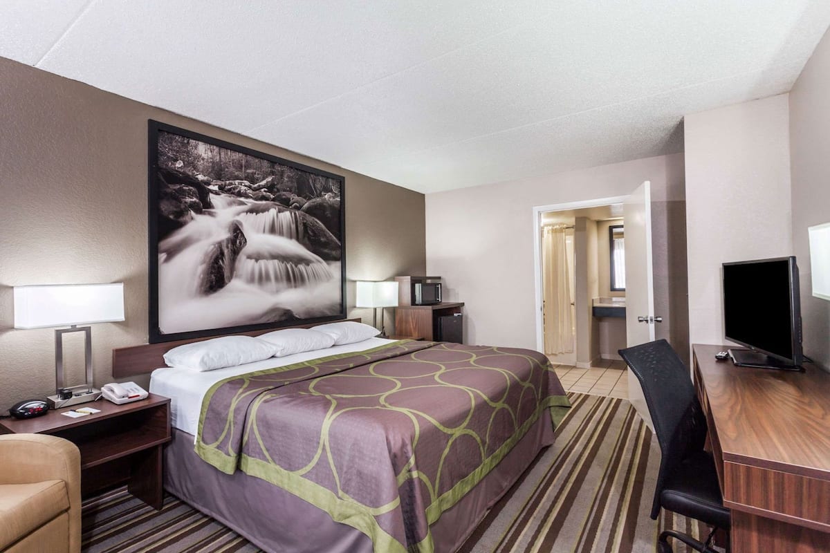 A hotel room with a bed, bedside lamps, a desk with a TV, and a large framed picture of a waterfall.