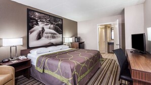 A hotel room with a bed, a desk, a TV, a lamp, and a painting of a waterfall. - Super 8 by Wyndham Pigeon Forge Dollywood Lane (Pigeon Forge)
