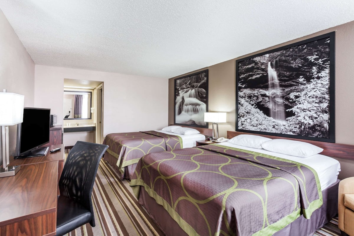 A hotel room with two beds, a desk with a computer, a chair, and a TV.