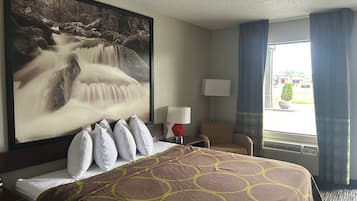 A hotel room with a bed, a large painting of a waterfall, a chair, a lamp, and a window with curtains.