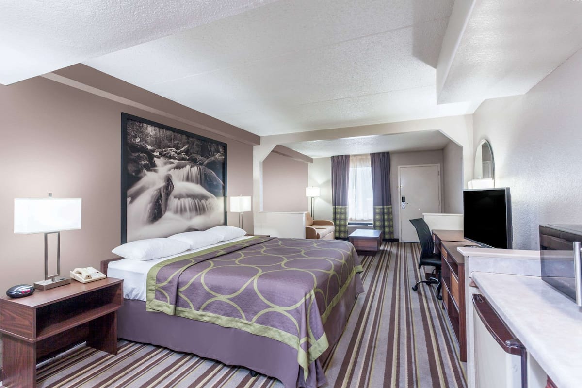 A hotel room with a bed, a desk, a chair, a TV, and a painting on the wall.