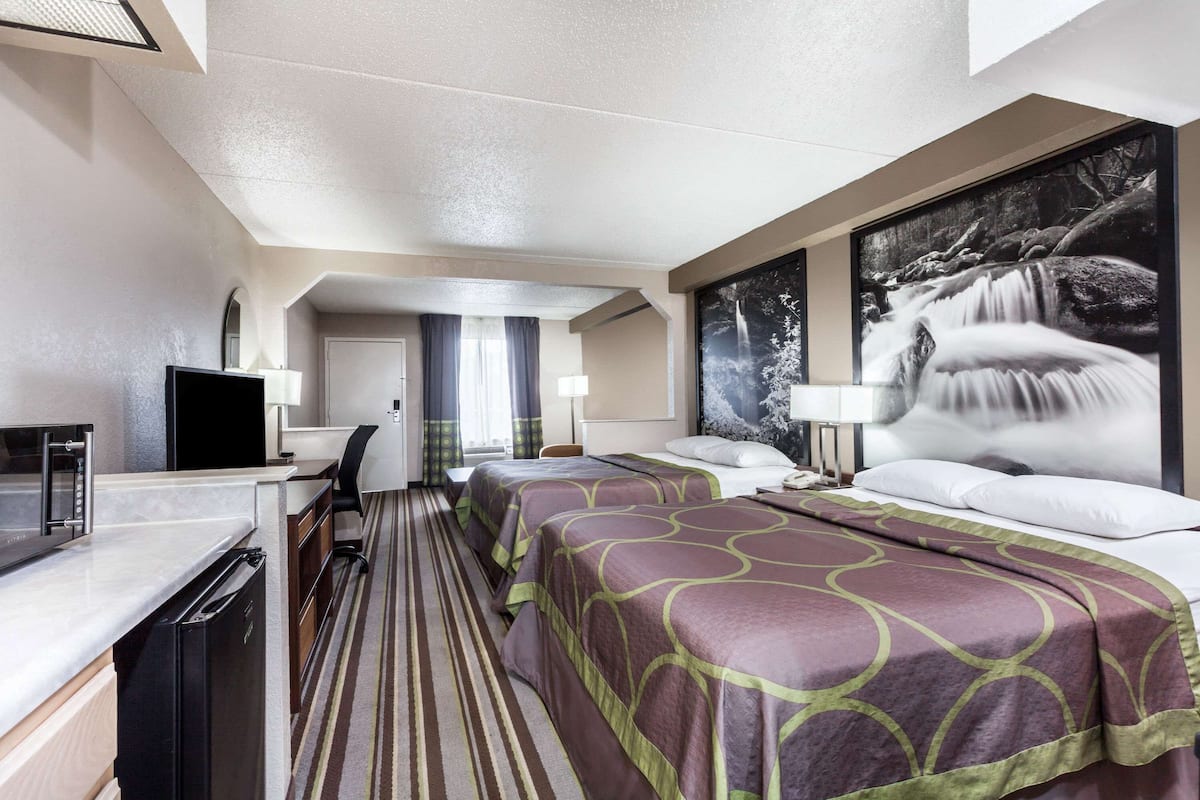 A hotel room with a kitchenette, two beds, a large window, and a waterfall painting.
