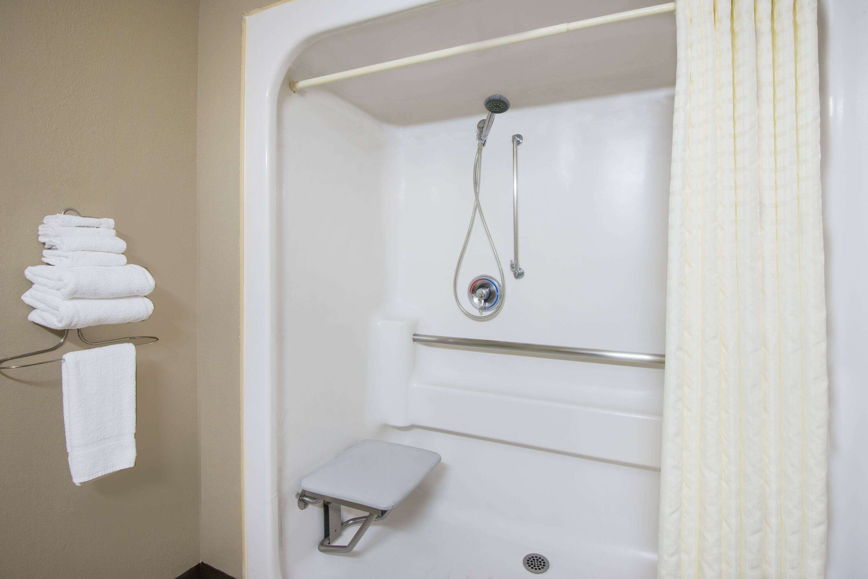A bathroom with a shower, a toilet, and a stack of towels on a rack.