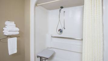 A bathroom with a shower, a toilet, and a stack of towels on a rack.