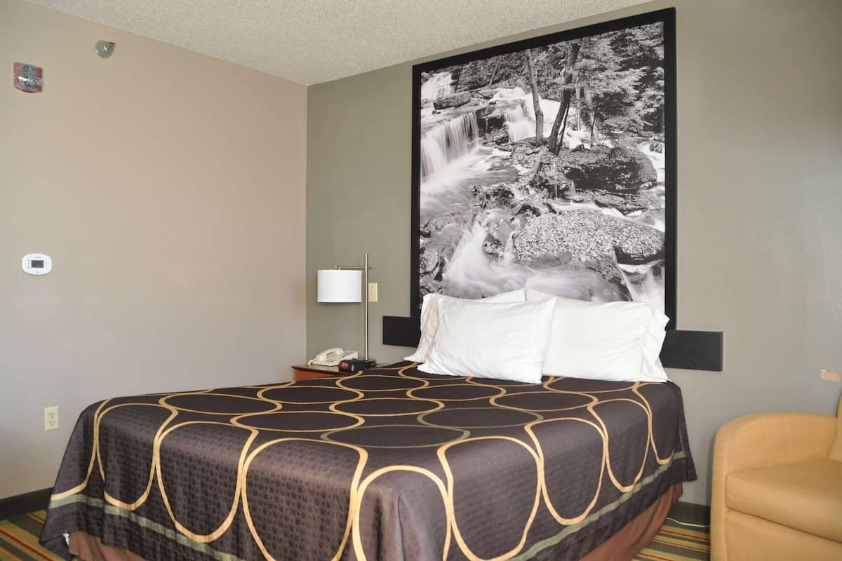 A hotel room with a large bed, a nightstand with a lamp, and a wall-mounted phone.