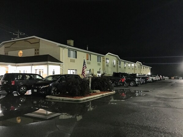 Un motel con estacionamiento, una bandera y varios vehículos estacionados.