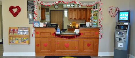 Un'area reception con un bancone in legno, una sveglia, una decorazione a forma di cuore, un bancomat e il cartello Super 8.