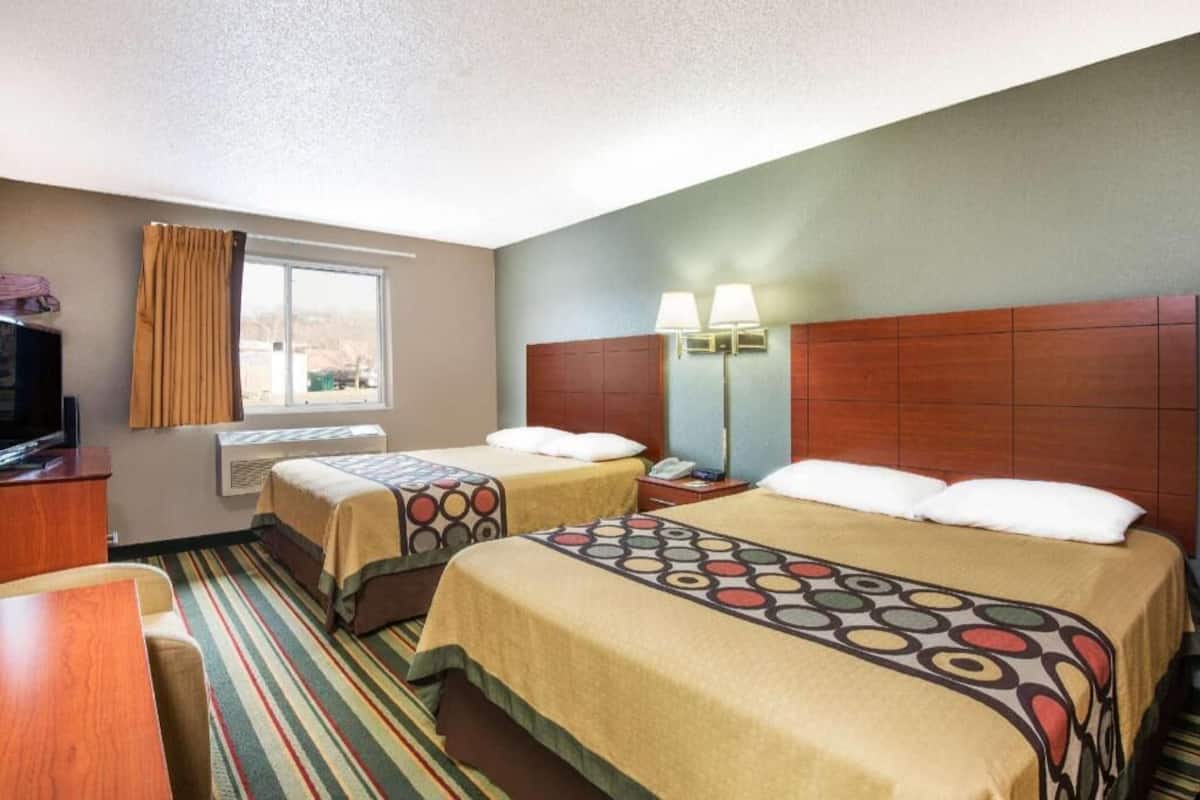 A hotel room with two beds, a TV, a desk, a window with curtains, and a lamp.