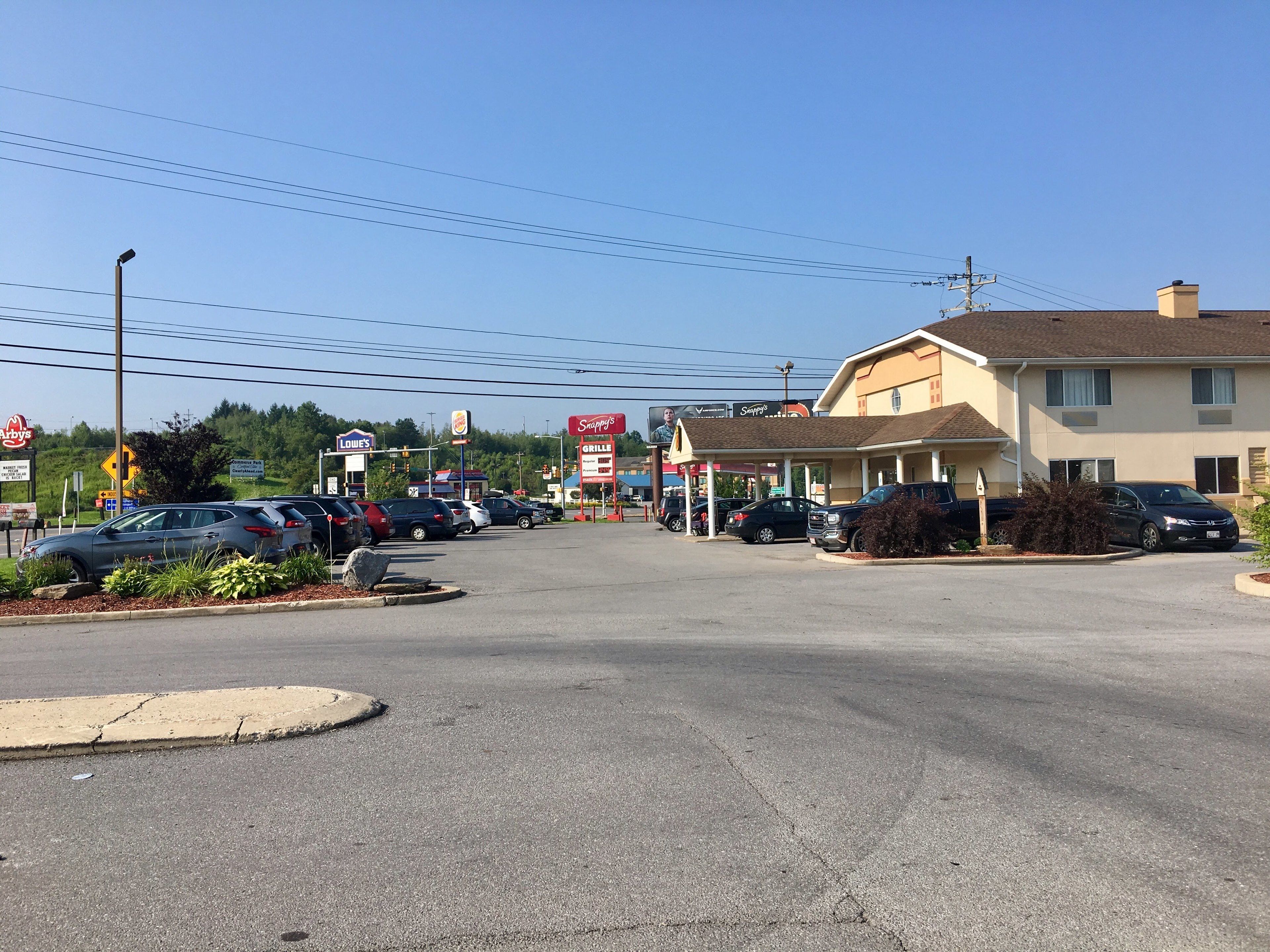 A parking lot with several cars, a building with a sign for 'Snappy's Grille', and a billboard advertising 'Arby's'.