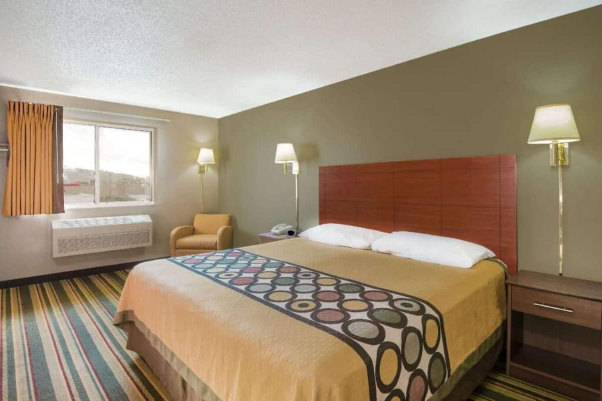 A hotel room with a bed, a chair, a desk, and a window.