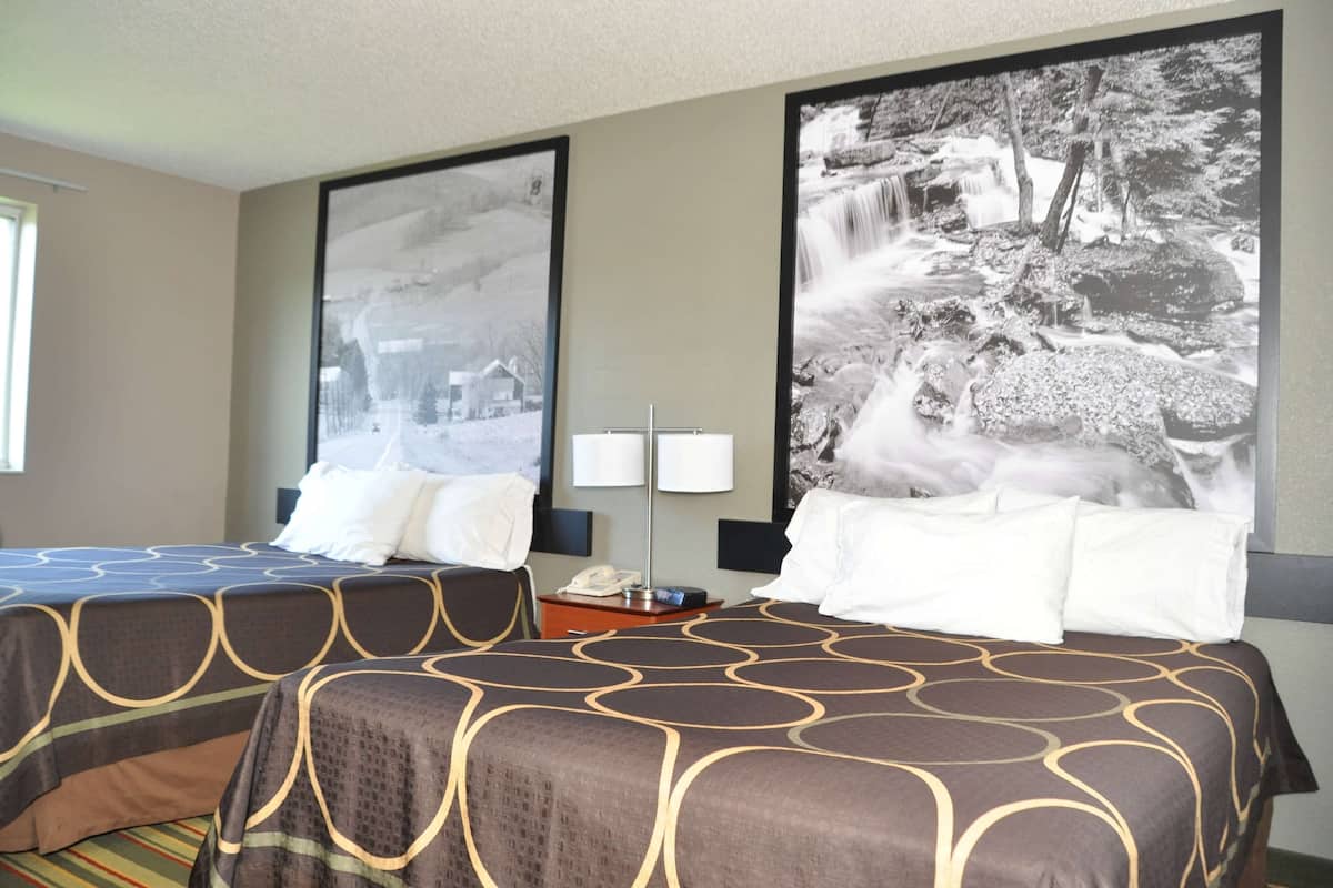 A hotel room with two beds, a nightstand, a lamp, and two large black-and-white photographs on the wall.